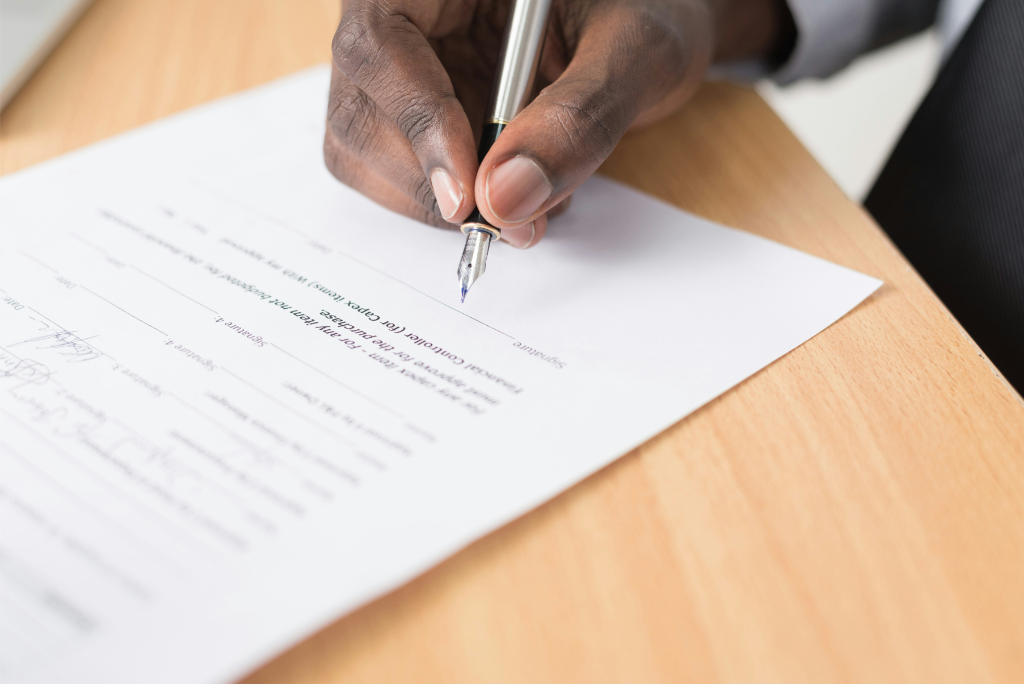 Une personne signe un document avec un stylo sur un bureau en bois, prenant des mesures réfléchies pour planifier sa succession.