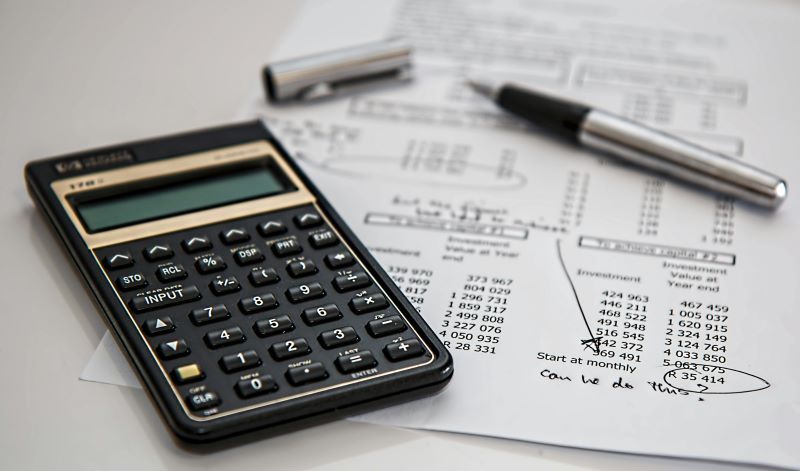 Une calculatrice et un stylo reposent sur un document contenant des chiffres et des calculs, illustrant la nature simple d'un système de flat tax.