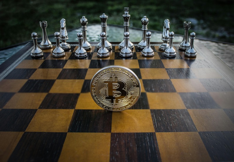 Une pièce Bitcoin se dresse sur un échiquier avec des pièces d'échecs en argent disposées en arrière-plan, symbolisant des mouvements stratégiques pour ceux qui cherchent à investir dans les cryptomonnaies en 2025.